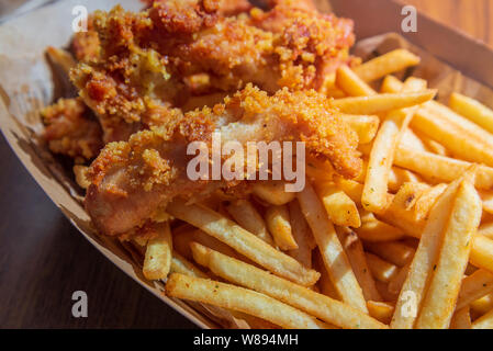 Haut de la vue de près et croustillant poulet frit croustillant sans os et pommes de terre rissolées avec katch jusqu'à côté, servir du bac à papier et table en bois. Banque D'Images