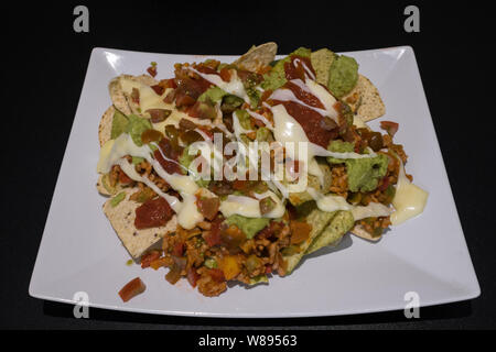 Nachos avec viande hachée, poivre, guacamole et fromage fondu sur une plaque sur un tableau noir Banque D'Images