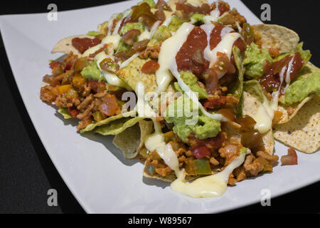 Nachos avec viande hachée, poivre, guacamole et fromage fondu sur une plaque sur un tableau noir Banque D'Images