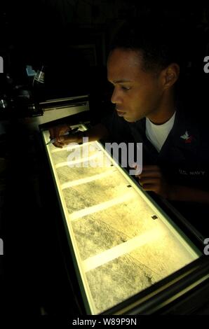 Maître de 2e classe Damon Jenkins reviews l'imagerie de reconnaissance aérienne sur une table lumineuse dans le navire transporteur Intelligence Center à bord de l'USS JOHN C. STENNIS (CVN 74) opérant dans l'océan Indien le 24 septembre 2004. L'imagerie est de F-14 Tomcat de l'Escadron de chasse 31 prise lors d'une reconnaissance aérienne tactique système Pod (bâches) mission. La bâche est utilisée pour fournir l'acquisition d'objectifs et d'identification, d'évaluation cible après la grève et la surveillance maritime d'imagerie. Jenkins est de Los Angeles, Californie. Banque D'Images