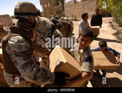 Un soldat de l'armée iraquienne mains une boîte de nourriture à un garçon de la tribu des Choloq Shababit dans um, l'Iraq, le 23 juin 2005. Les soldats de l'armée iraquienne, 3e Bataillon, 4e compagnie de l'armée américaine et le 3e régiment de cavalerie blindée a distribué des fournitures humanitaires, l'eau et la nourriture aux membres de la tribu. Banque D'Images