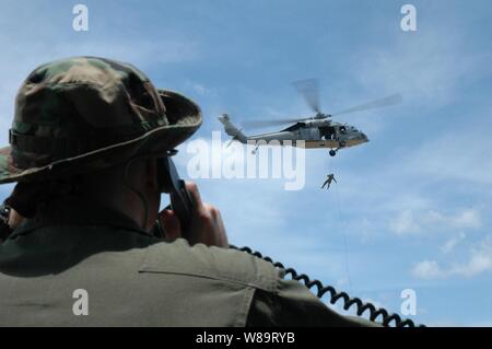 La Marine américaine Maître de 2e classe Justin Birch utilise une radio portable pour parler aux pilotes d'un hélicoptère Seahawk MH-60S comme un technicien des explosifs et munitions de la Marine royale australienne repousse de l'hélicoptère à Santa Rita, Guam, le 19 avril 2006. Les marins des deux marines de la formation dans les techniques de suspension corde d'hélicoptères à Santa Rita.