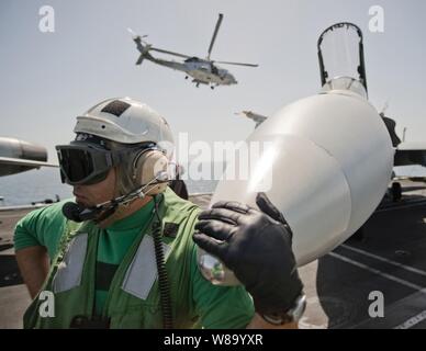 Le premier maître de Todd aile, affecté à l'escadron de combat interarmées 25, attend avec un F/A-18C Hornet que c'est préparé pour une mission sur le pont du porte-avions USS Carl Vinson (CVN 70) en cours dans la mer d'Oman le 9 mars 2011. Le groupe aéronaval du Carl Vinson est déployé des opérations de sécurité maritime et les efforts de coopération en matière de sécurité dans le théâtre dans la 5e Flotte des États-Unis zone de responsabilité. Banque D'Images