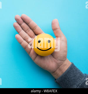 Mele hand holding ball émoticône jaune sur fond de couleur bleu Banque D'Images