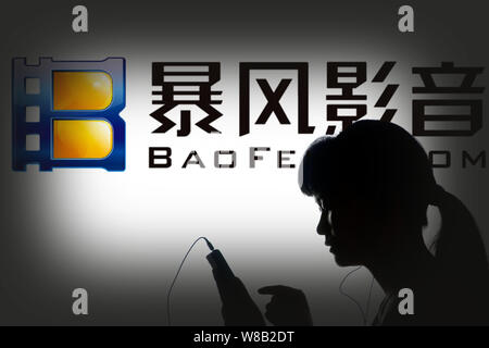 --FILE--Une femme chinoise utilise son téléphone mobile devant une publicité pour Baofeng.com de technologie Chongde de Shaoyang, Chine centrale's Hun Banque D'Images