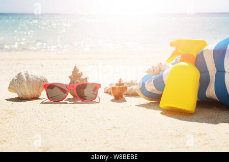 Lunettes de soleil en face de coquillage près de sac à main et jaune flacon pulvérisateur sur Sand At Beach Banque D'Images