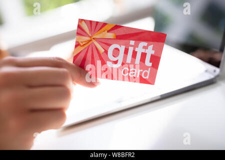 Close-up of Woman's Hand Holding Red Gift Card tout en tapant sur l'ordinateur portable Banque D'Images