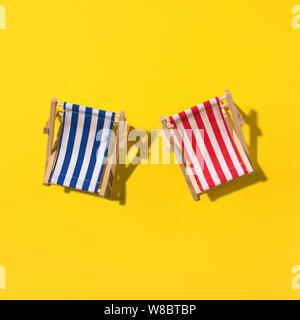 Deux chaises longues avec ombre, monstera et de feuilles de palmier sur du papier jaune arrière-plan. Mise à plat et de copier l'espace. Été voyage vacances concept. Composition minimale. Banque D'Images