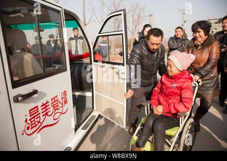 --FILE--fermier chinois Ma Xiaopeng, centre, ouvre la porte d'un véhicule électrique offert par une entreprise avant d'envoyer son épouse paralysée Zhang Guilin Banque D'Images