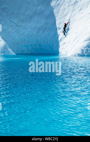 Femme escalade de glace au-dessus de l'eau d'un bleu profond d'un lac glaciaire sur le Glacier Matanuska en Alaska. Banque D'Images