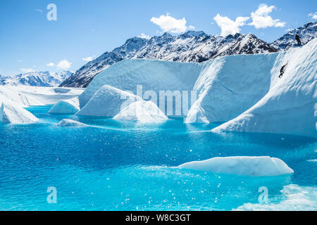 Grimpeur sur glace ordre croissant un mur de glace vers leur guide d'escalade, au-dessus d'un lac d'un bleu profond sur la Matanuska Glacier en Alaska. Banque D'Images