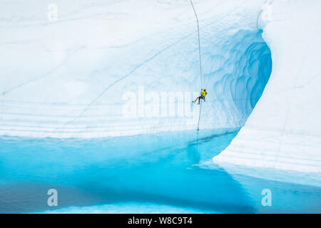 Jeune homme rappels devant une grande caverne de glace sur le Glacier Matanuska. La cave est inondée par un lrage blue piscine ou lac supraglaciaire. Banque D'Images