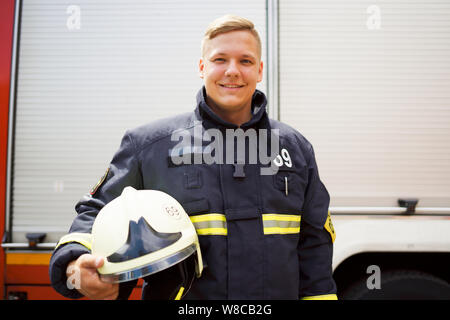 Photo de heureux pompier avec casque dans sa main, debout près de fire truck Banque D'Images