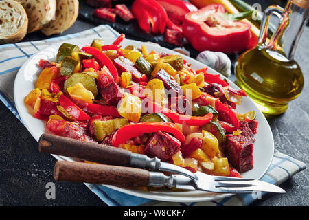 Pisto manchego espagnol - Ragoût aux légumes avec saucisses chorizo frit servi sur une plaque blanche sur une table en béton avec des tranches de pain, vue de dessus, cl Banque D'Images