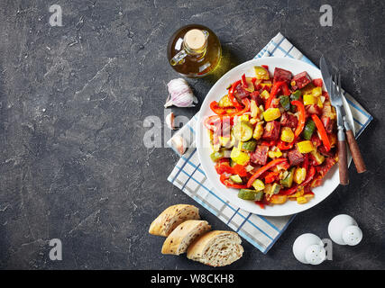 Pisto manchego espagnol - Ragoût aux légumes avec saucisses chorizo frit servi sur une plaque blanche sur une table en béton avec des tranches de pain, vue de dessus, cl Banque D'Images