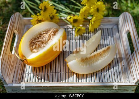 Couper le melon Oriental jaune (melon) Coréen sur un plateau en bois blanc Chrysanthème jaune sur l'arrière-plan. Banque D'Images