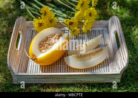 Couper le melon Oriental jaune (melon) Coréen sur un plateau en bois blanc Chrysanthème jaune sur l'arrière-plan. Banque D'Images