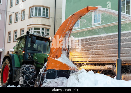 Grand tracteur avec des chaînes sur les roues de la poudrerie à partir de la rue de ville en dump truck body. Le nettoyage des rues et l'enlèvement de la neige après chute de neige. Administration municipale Banque D'Images