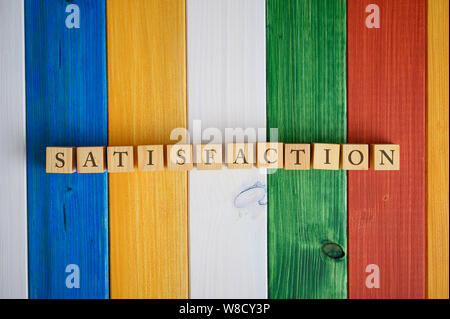 Vue de dessus de cubes en bois dans une rangée l'orthographe du mot satisfaction. Plus de 24 couleurs de planches de bois. Banque D'Images