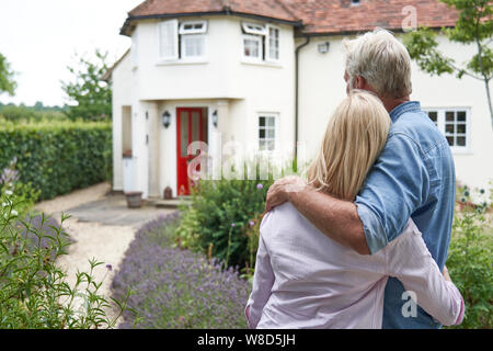Vue arrière du Couple Standing In Garden Regarder Maison de rêve en campagne Banque D'Images