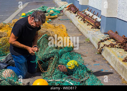 8 Août 2019 Un homme d'âge moyen à genoux sur le trottoir alors qu'il raccommode les filets de pêche à quai dans le port de Douarnenez le comté de Down en Irlande du Nord Banque D'Images