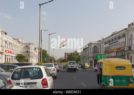 Les véhicules qui circulent sur route avec drapeau indien en arrière-plan à Connaught Place à New Delhi Banque D'Images