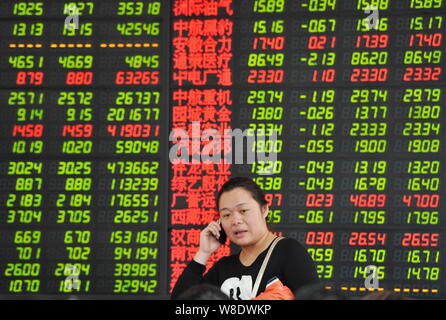 Un investisseur chinois parle sur son téléphone mobile devant un écran affichant les prix des actions (rouge pour l'augmentation des prix et la baisse des prix vert) à un st Banque D'Images