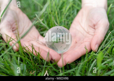Sauver la Terre consept. Concept de l'environnement. Bille de verre de femmes sur le palm. fond d'herbe verte Banque D'Images