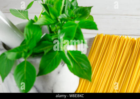 Feuilles de basilic vert dans un mortier en marbre et des pâtes sur une table en bois blanc, close-up Banque D'Images