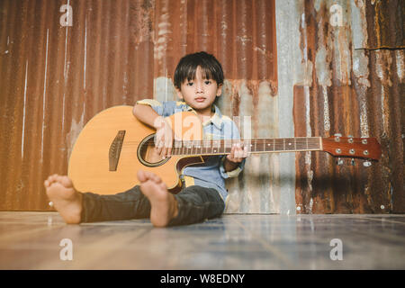 Asian boy playing acoustic guitar avec de vieux fond acier Banque D'Images