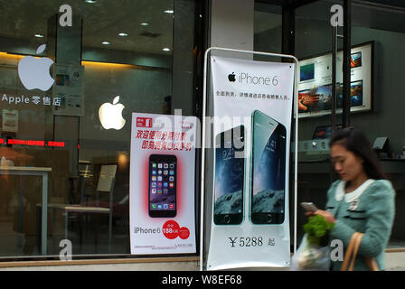 --FILE--un piéton utilise son téléphone portable pendant qu'elle passe devant une publicité pour l'iPhone 6 et 6 smartphones plus dans un Apple store à Yichang city, c Banque D'Images