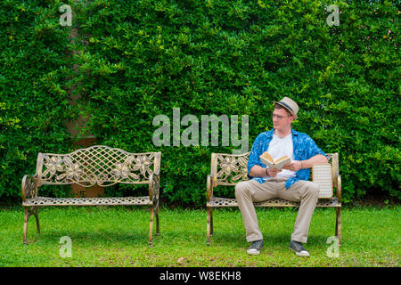 Caucasian man assis sur la chaise et de la lecture livre dans le jardin Banque D'Images