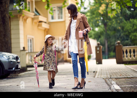 Mère et fille heureux aller à l'école élémentaire. En mère enfant à l'école primaire. Rendez-vous avec l'étude de l'élève à dos. Banque D'Images