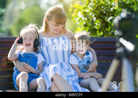 Une belle femme avec deux filles est tourné dans un programme TV, est assis en face d'un appareil photo sur le banc de parc. Banque D'Images