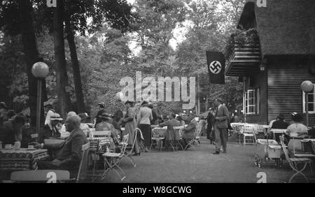 Les gens à un out-door restaurant en Allemagne avant l'outberak de la Seconde Guerre mondiale, avec le drapeau à croix gammée nazie avec emblème en bonne place sur l'écran, 1930 Banque D'Images