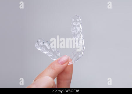 Close-up of Woman's Hand Holding accolades en plastique transparent sur fond gris Banque D'Images
