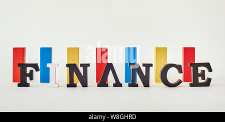 Blocs de bois rouges, bleus et jaunes de même hauteur sur fond blanc. Word Finance fait de lettres en bois debout dans une rangée. Tir horizontal Banque D'Images