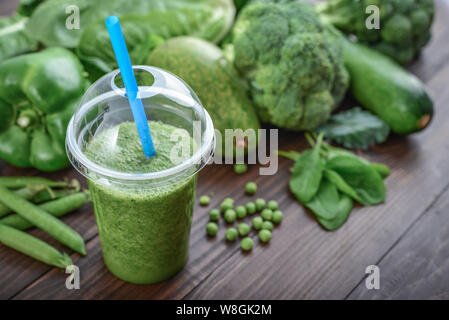 Smoothie vert mélangé dans la tasse en plastique avec des ingrédients sur la table en bois Banque D'Images