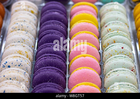 Macarons français sont disposés en rangées de lisse blanc rose violet. Pâte à macaron gâteaux à la crème, les biscuits sucrés showcase confiserie Banque D'Images