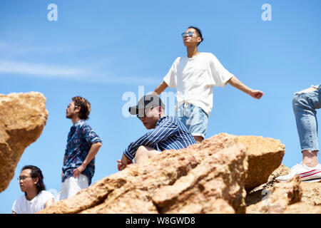 Groupe de jeunes adultes asiatiques hommes debout sur le haut des roches contre ciel bleu profitant du soleil et de l'air frais Banque D'Images