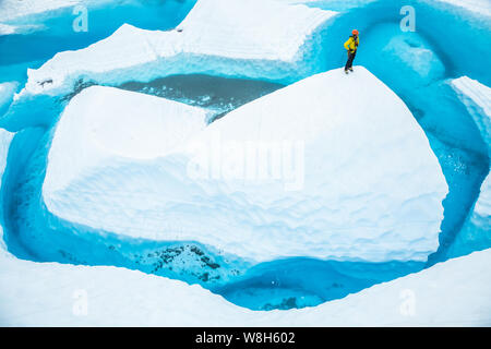 Après l'équitation dans un canoë, un jeune homme se dresse au sommet d'un sérac ou fin de glace qui sort d'une gigantesque piscine bleu. Le lac supraglaciaire repose sur le dessus Banque D'Images