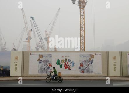 --FILE--un cycliste chevauche son vélo électrique passé un site de construction en gros le smog à Pékin, Chine, 19 novembre 2014. Le Conseil d'État a émis un Banque D'Images