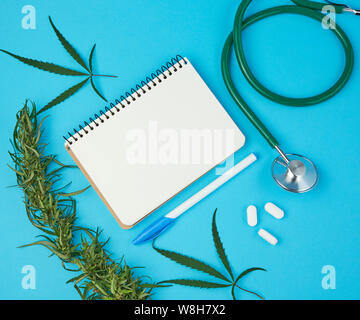 Ordinateur portable ouvert blanc avec des feuilles vierges, brindille de chanvre avec des feuilles vertes sur fond bleu, concept de la médecine alternative, la place pour l'écriture d'une prescrip Banque D'Images