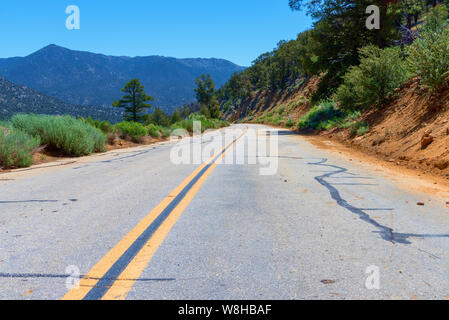 Tout droit en bas de la colline étroite route de montagne avec double lignes jaunes sous ciel bleu. Banque D'Images