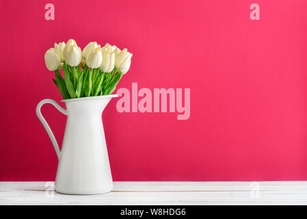 Bouquet de tulipes blanches en pot émaillé blanc sur fond rose Banque D'Images