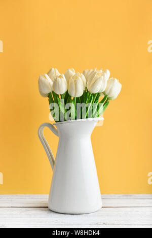 Bouquet de tulipes blanches en pot émaillé blanc sur fond jaune Banque D'Images