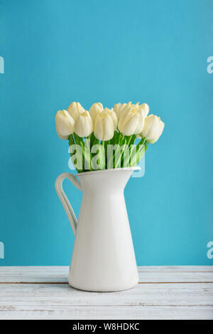 Bouquet de tulipes blanches en pot émaillé blanc sur fond bleu Banque D'Images