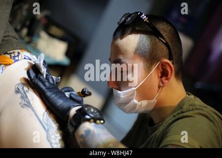 Artiste de tatouage chinois Wang Wenbin encres la cuisse d'un client dans un studio de tatouage à Shanghai, Chine, 29 mars 2015. Dans un studio de tatouage à Shanghai, Banque D'Images