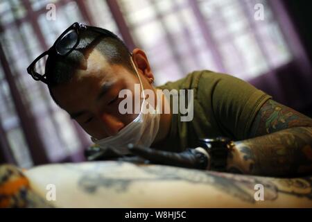 Artiste de tatouage chinois Wang Wenbin encres la cuisse d'un client dans un studio de tatouage à Shanghai, Chine, 29 mars 2015. Dans un studio de tatouage à Shanghai, Banque D'Images