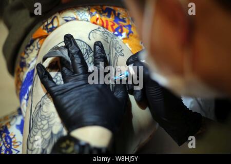 Artiste de tatouage chinois Wang Wenbin encres la cuisse d'un client dans un studio de tatouage à Shanghai, Chine, 29 mars 2015. Dans un studio de tatouage à Shanghai, Banque D'Images